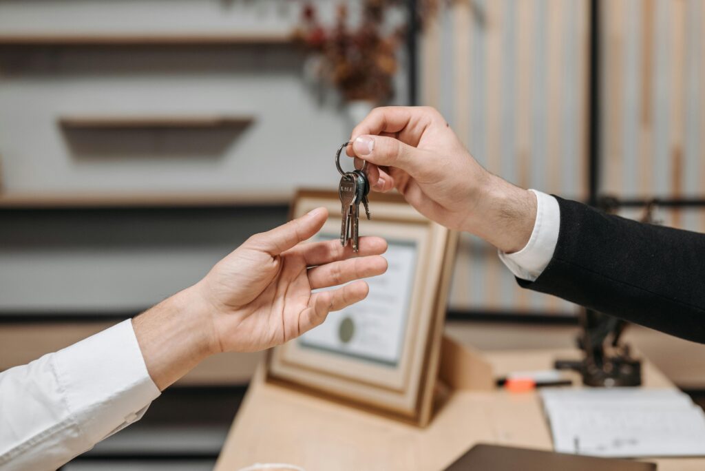 Detailed view of hands exchanging keys in a professional office environment, symbolizing real estate or business transactions.